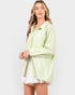 Woman wearing a light green ribbed cardigan over a white dress on a white background