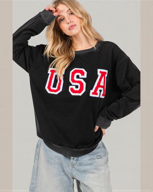 Woman wearing a black sweatshirt with 'USA' printed on it against a plain background