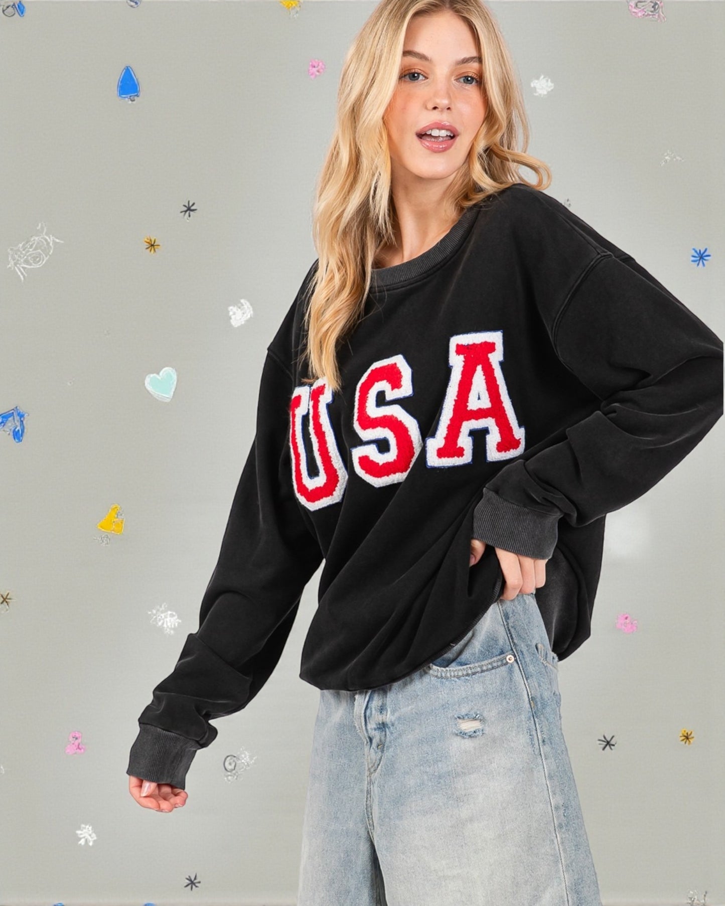 Person wearing a black sweatshirt with 'USA' printed in red and white on a gray background.