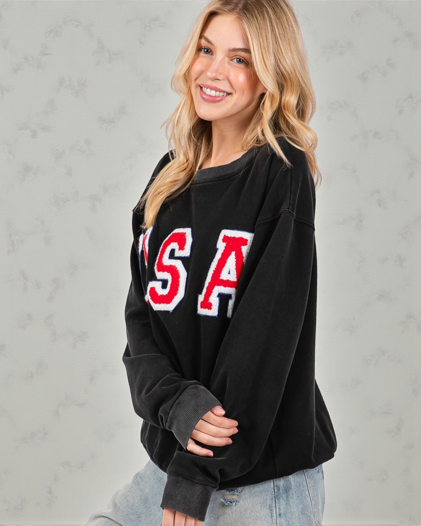 Woman wearing a black sweatshirt with 'USA' printed on it against a gray background