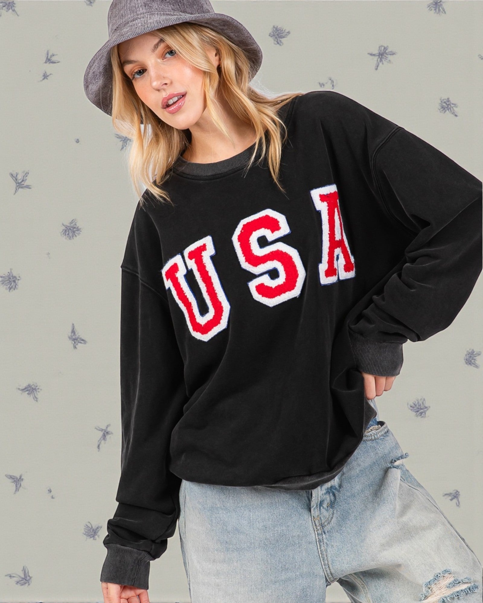 Person wearing a black sweatshirt with 'USA' printed in red and white, standing against a light background.
