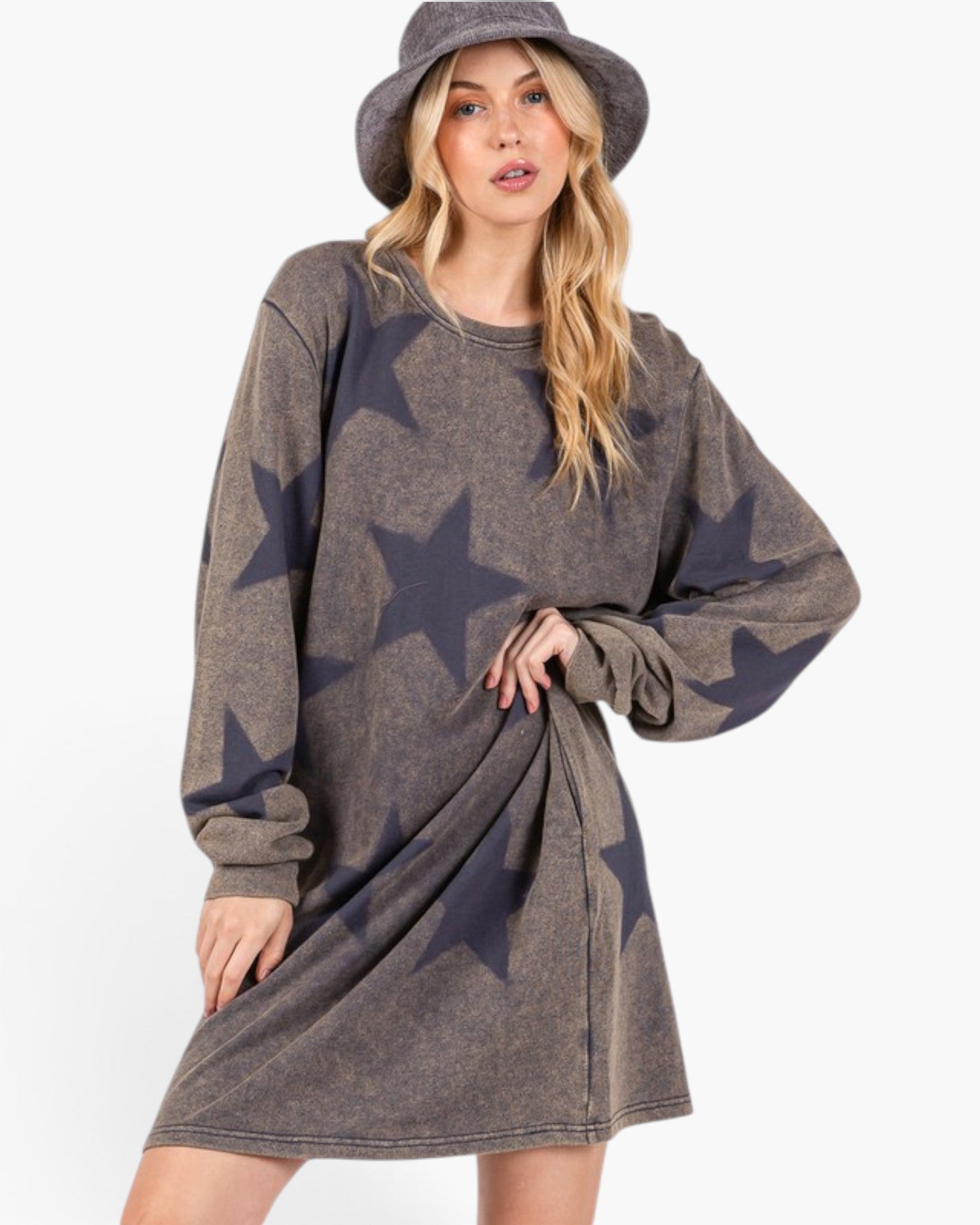A woman wearing a faded charcoal gray oversized sweatshirt dress with dark navy star prints, styled with a matching gray hat, against a plain white background.