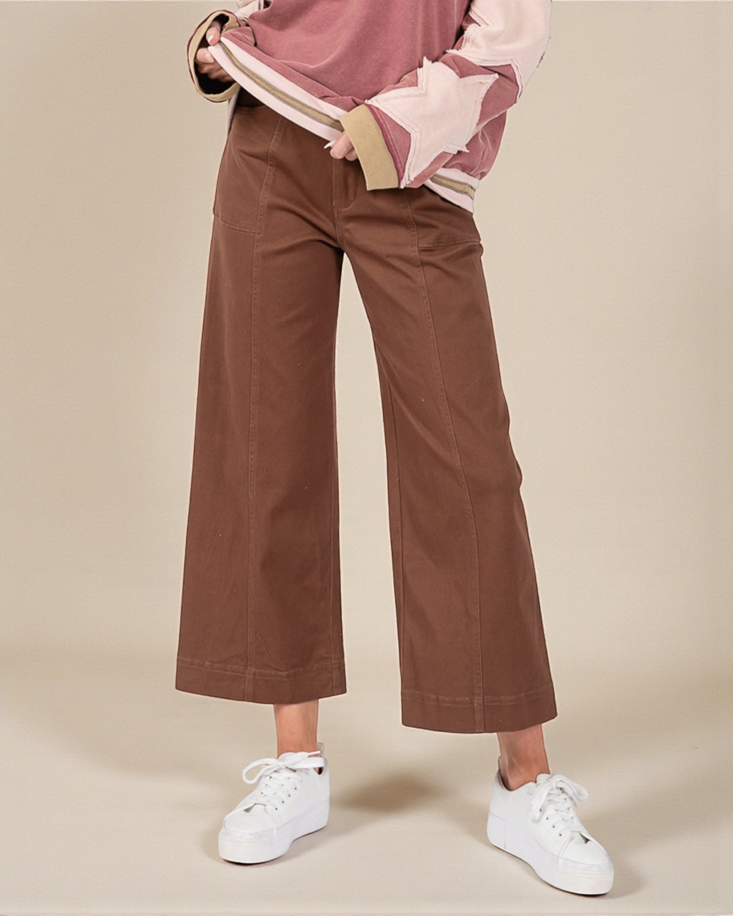 Person wearing brown wide-leg pants and a pink top on a beige background
