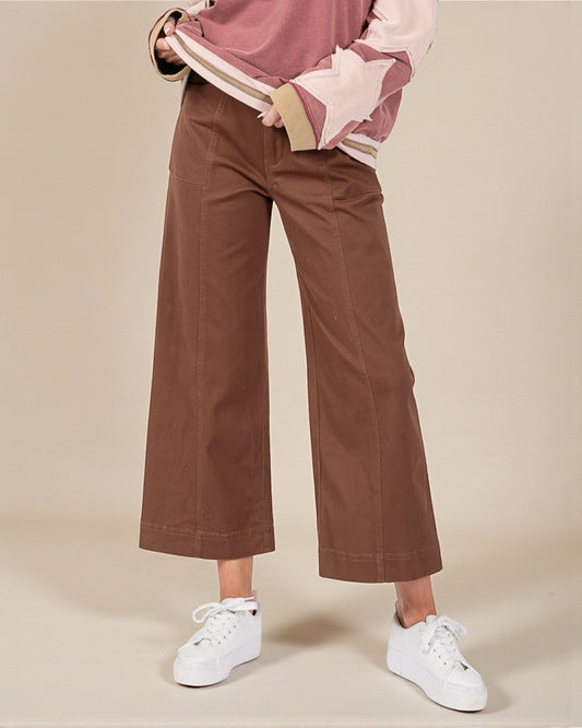 Person wearing brown wide-leg pants and a pink top on a beige background