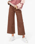 A model wearing brown wide-leg cropped pants, styled with a pink and beige striped jacket and white sneakers, against a plain white studio background.