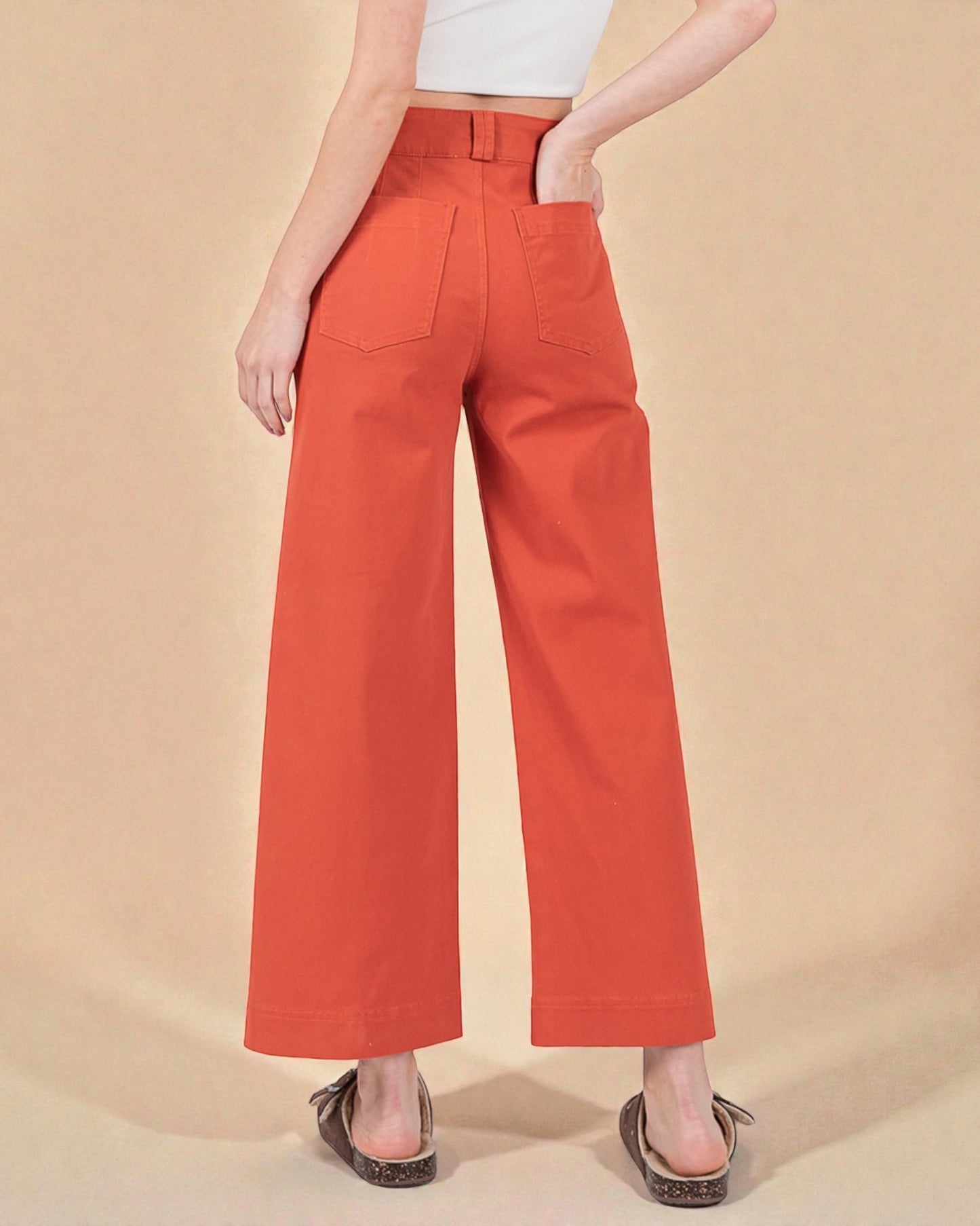 Person wearing orange wide-leg pants on a beige background