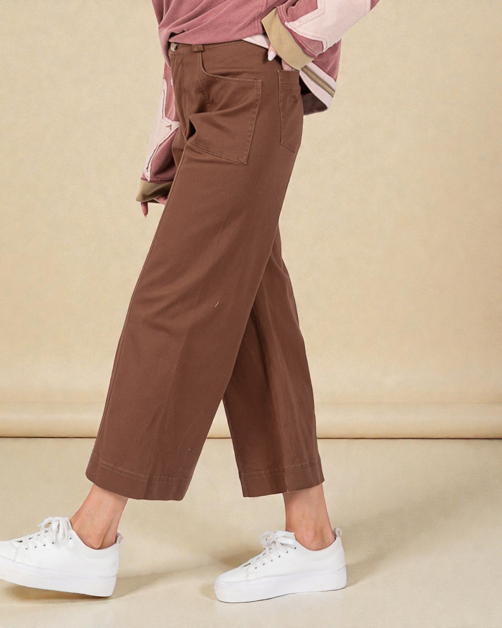 Brown wide-leg pants worn with a pink jacket and white sneakers on a beige background