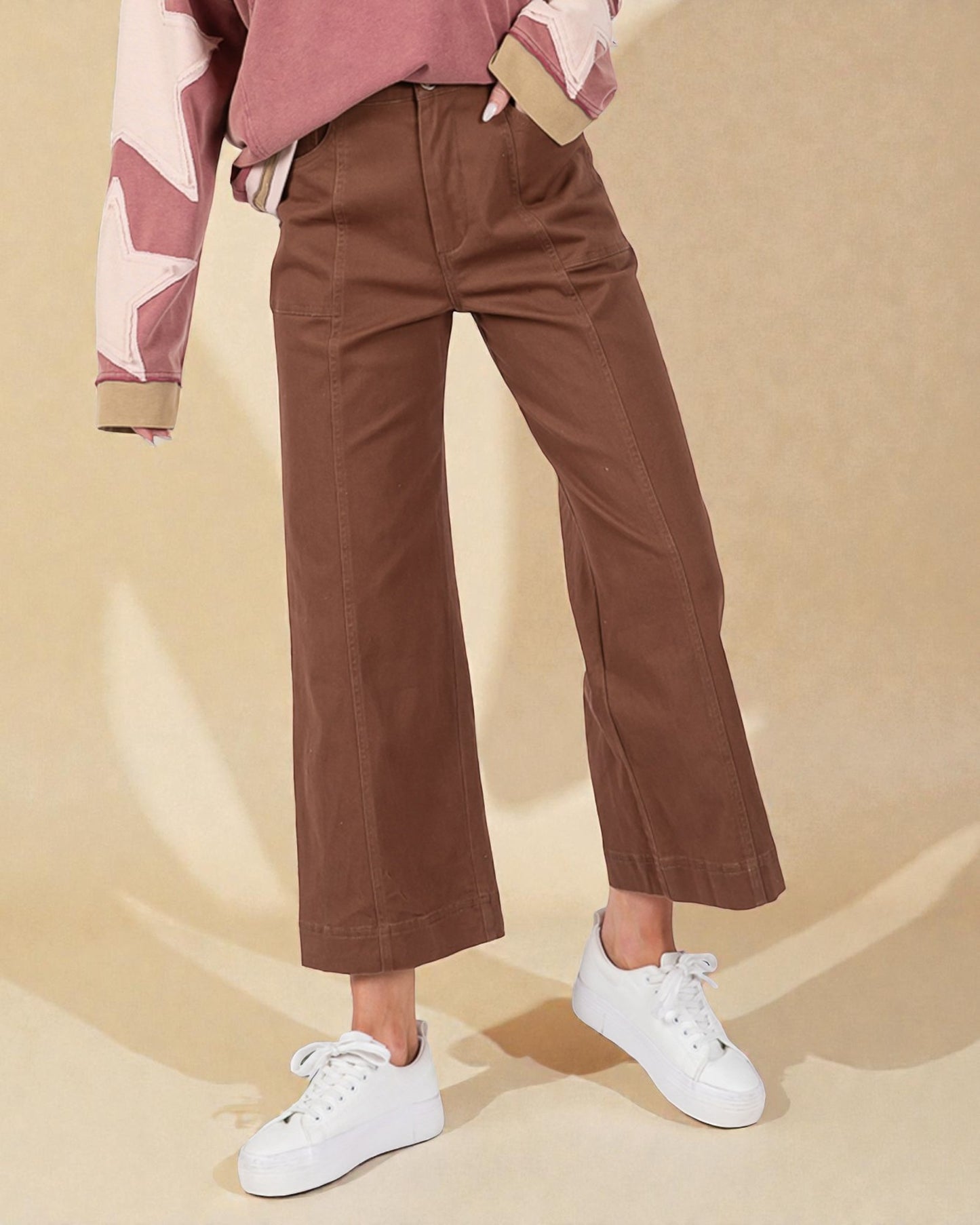 Person wearing brown pants and white sneakers on a beige background