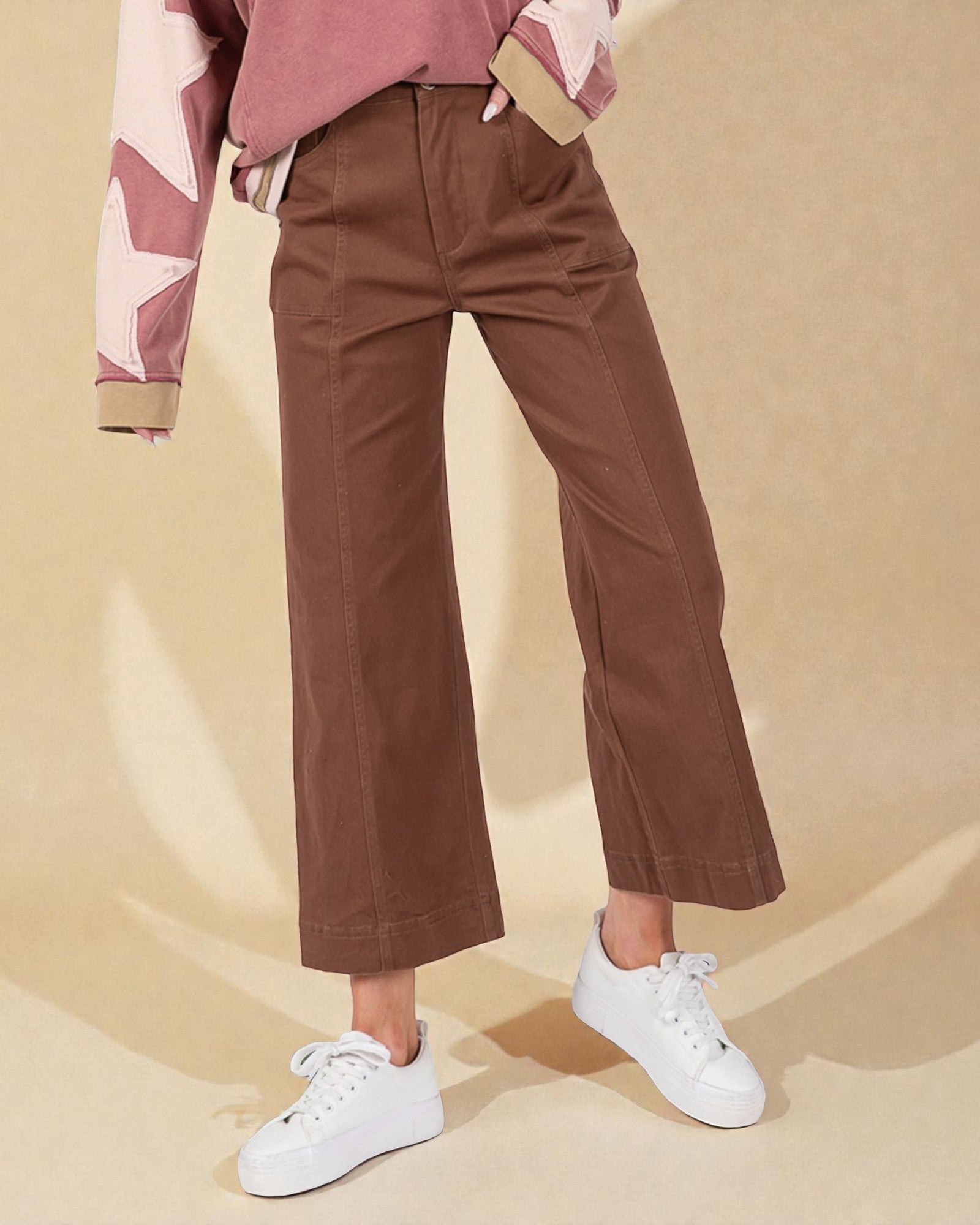 Person wearing brown pants and white sneakers on a beige background