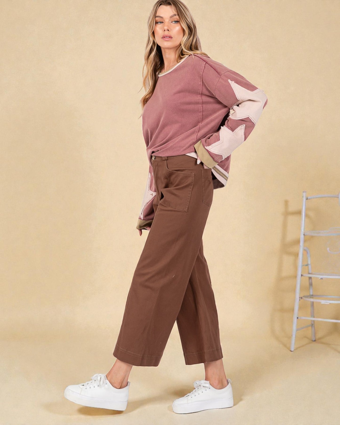 Woman wearing a pink sweater with star patterns and brown pants on a beige background