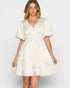 Woman wearing a white patterned dress on a plain background