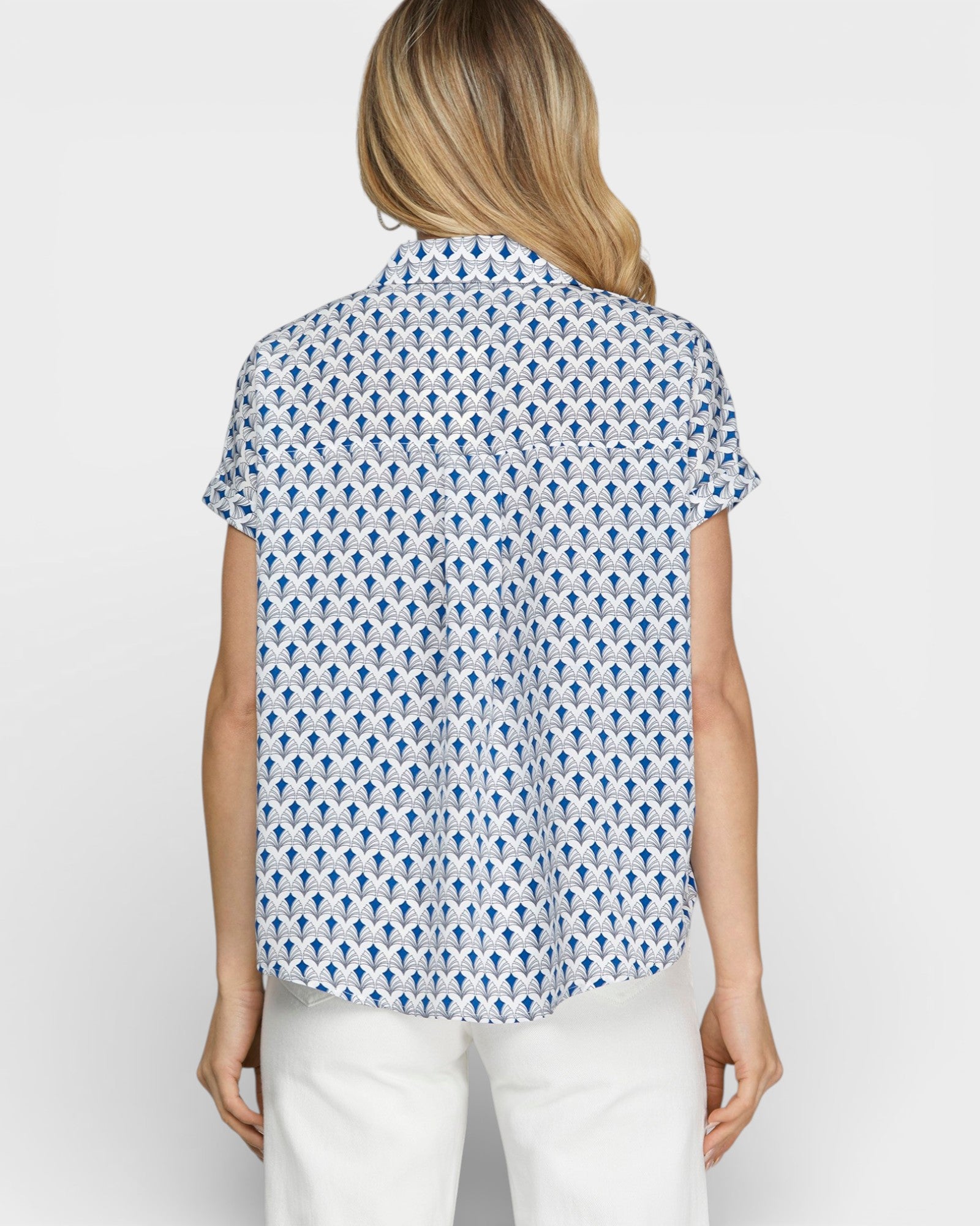 Woman wearing a blue patterned shirt and white pants on a plain background