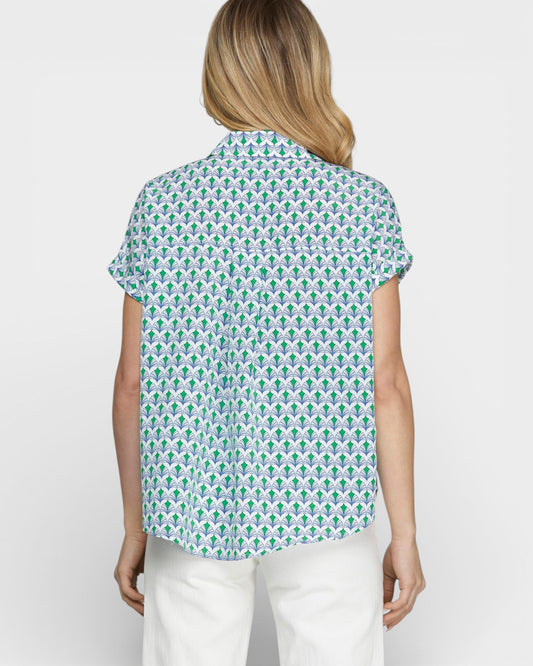 Woman wearing a patterned shirt and white pants on a plain background