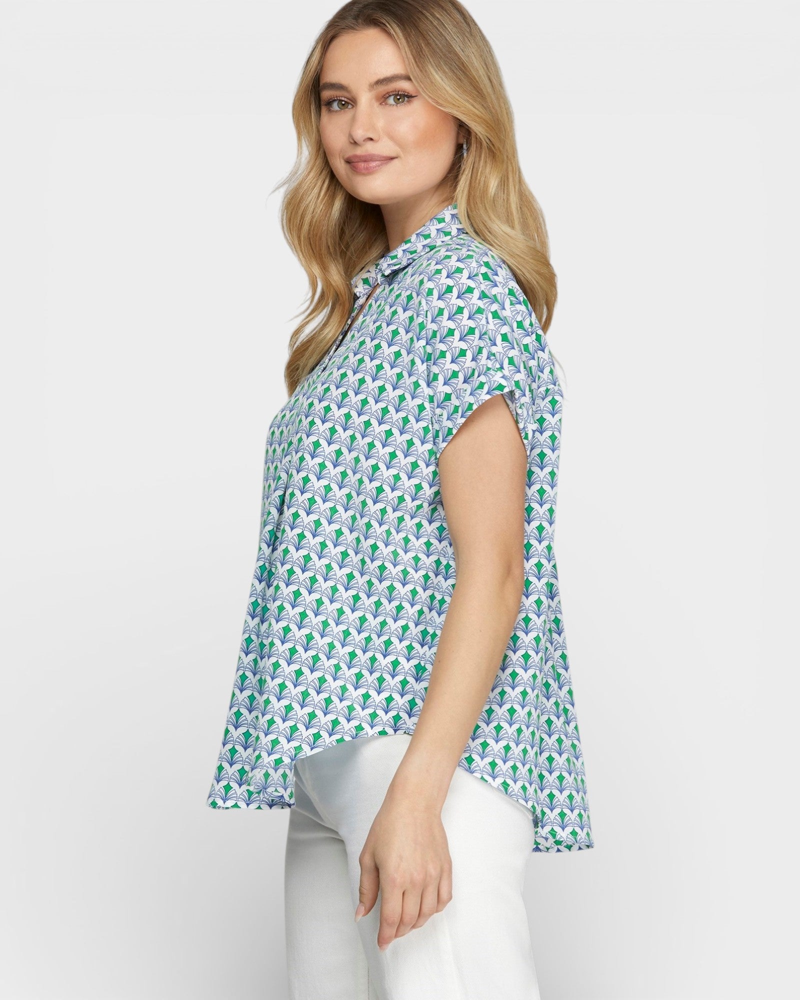 Woman wearing a patterned shirt and white pants on a plain background