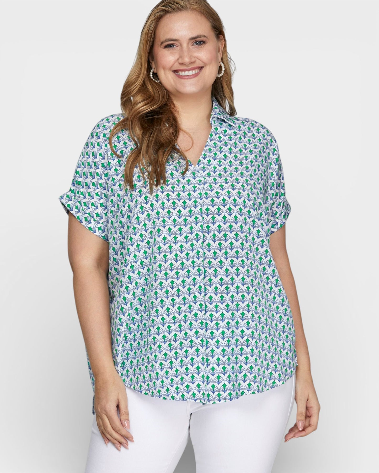 Woman wearing a green patterned shirt and white pants on a plain background