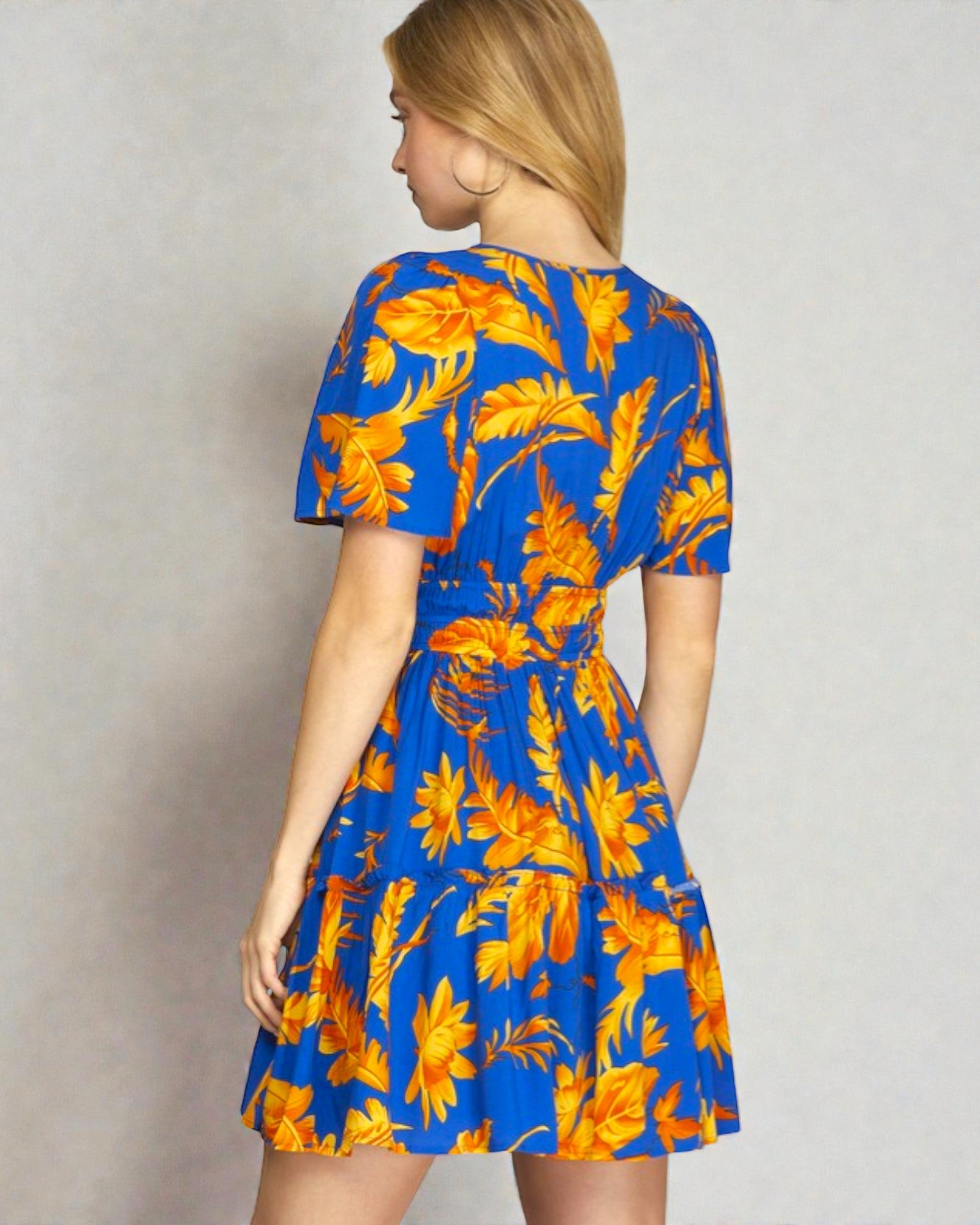Woman wearing a blue dress with orange floral pattern against a plain background