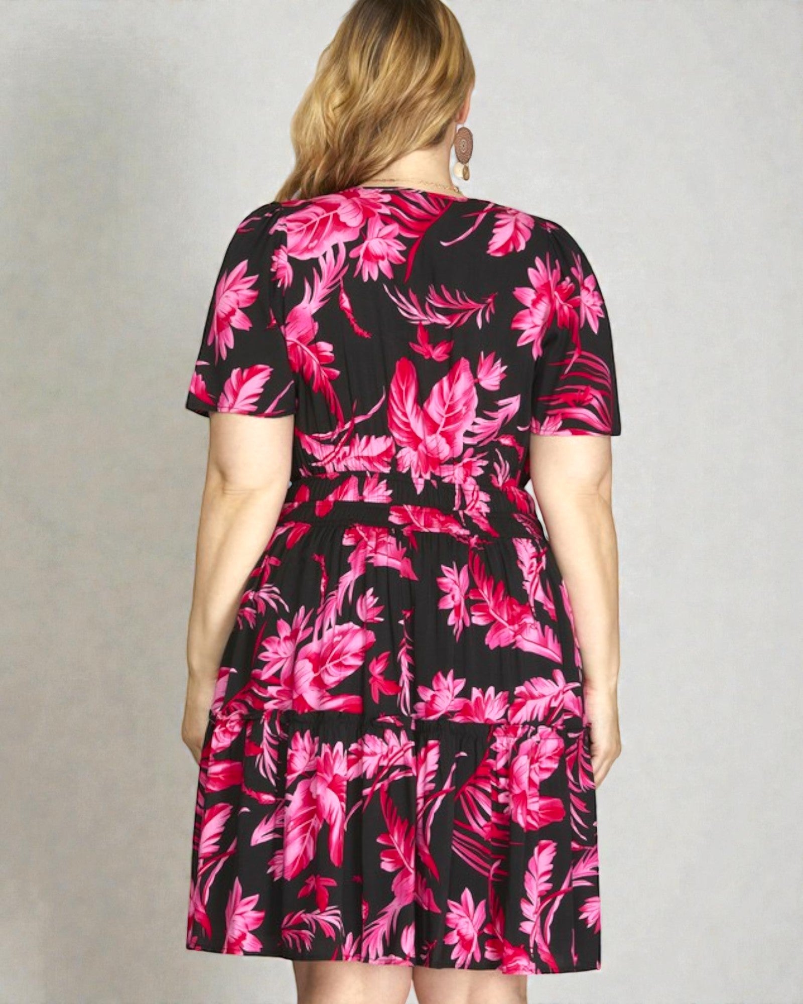 Woman wearing a black dress with pink floral pattern against a plain background