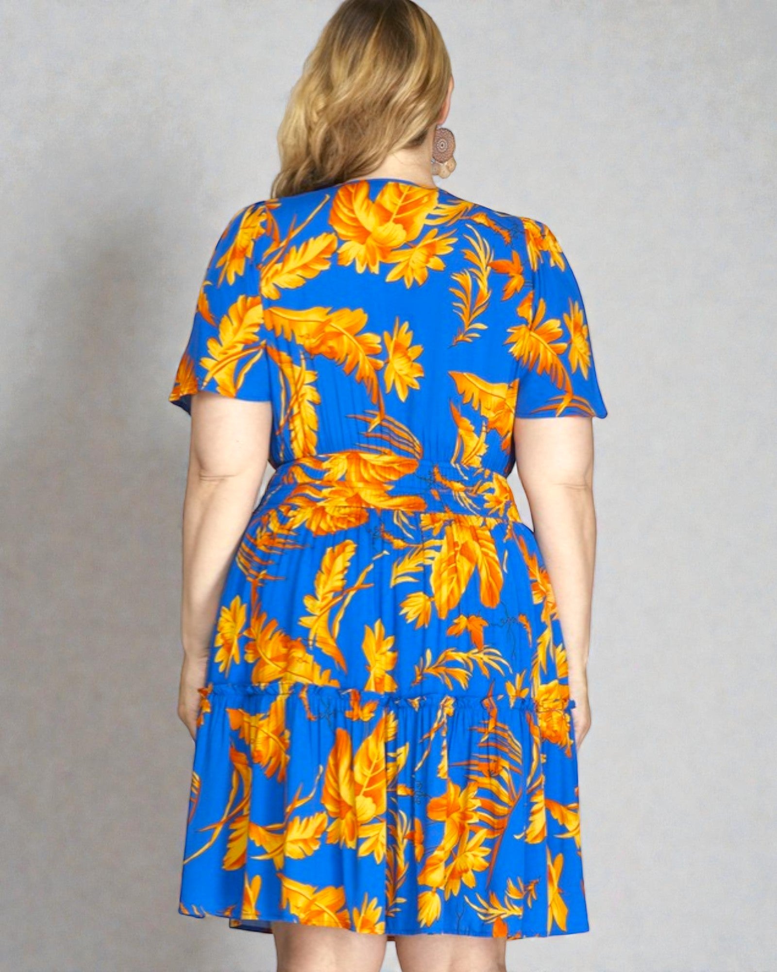 Woman wearing a blue dress with orange floral pattern against a gray background