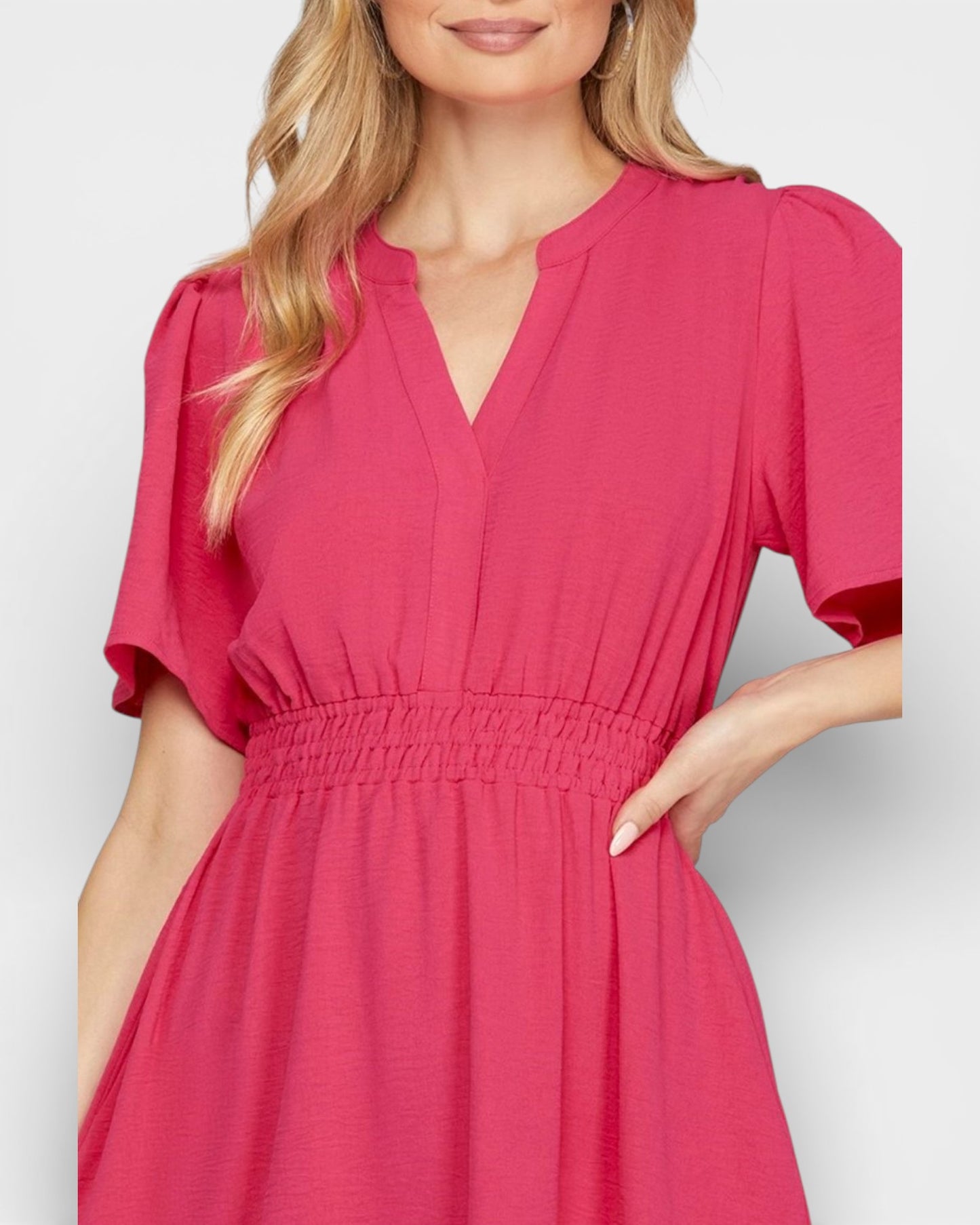 Woman wearing a pink dress with puff sleeves on a light gray background