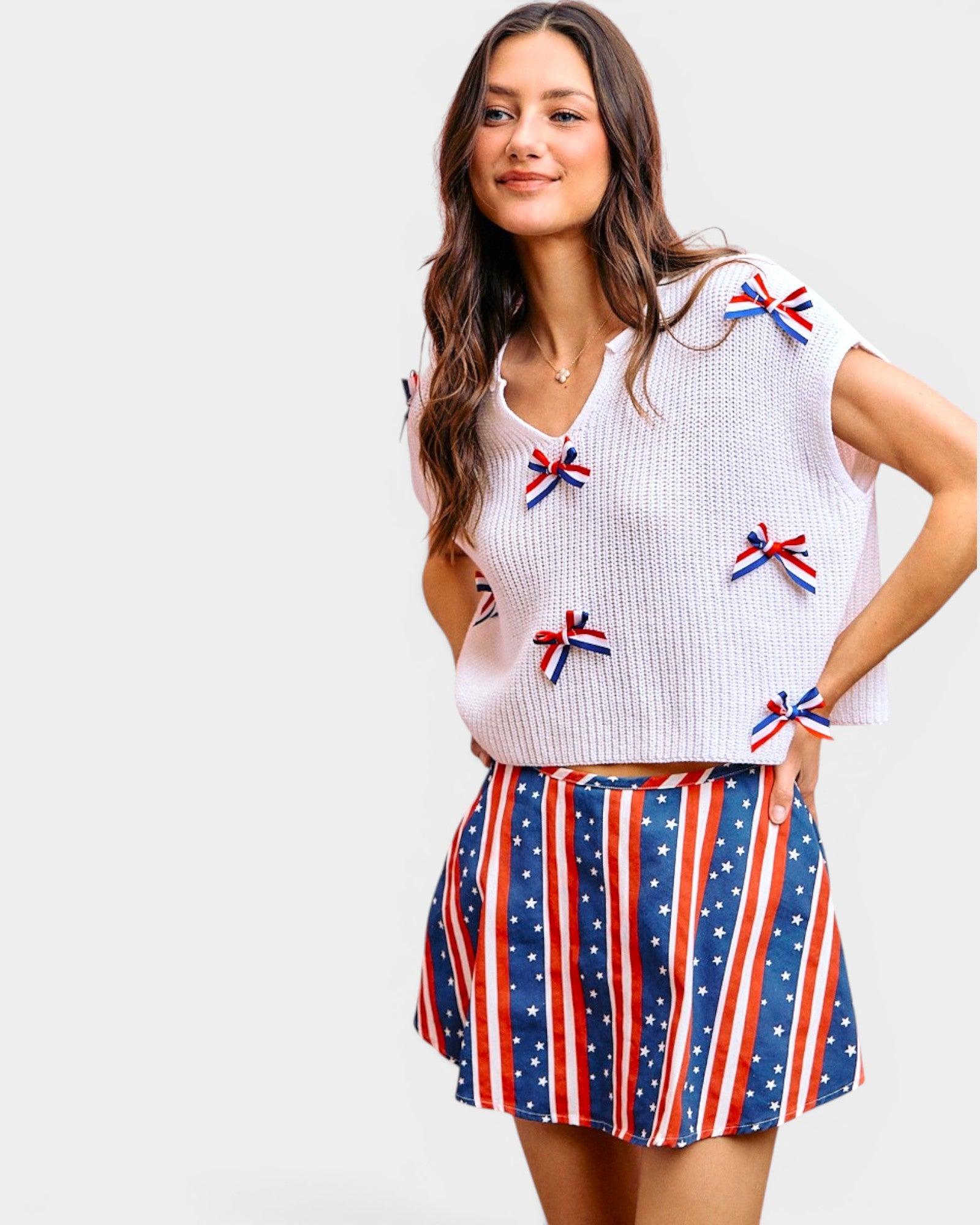 Woman wearing a white top with small flag designs and a red, white, and blue skirt on a light gray background