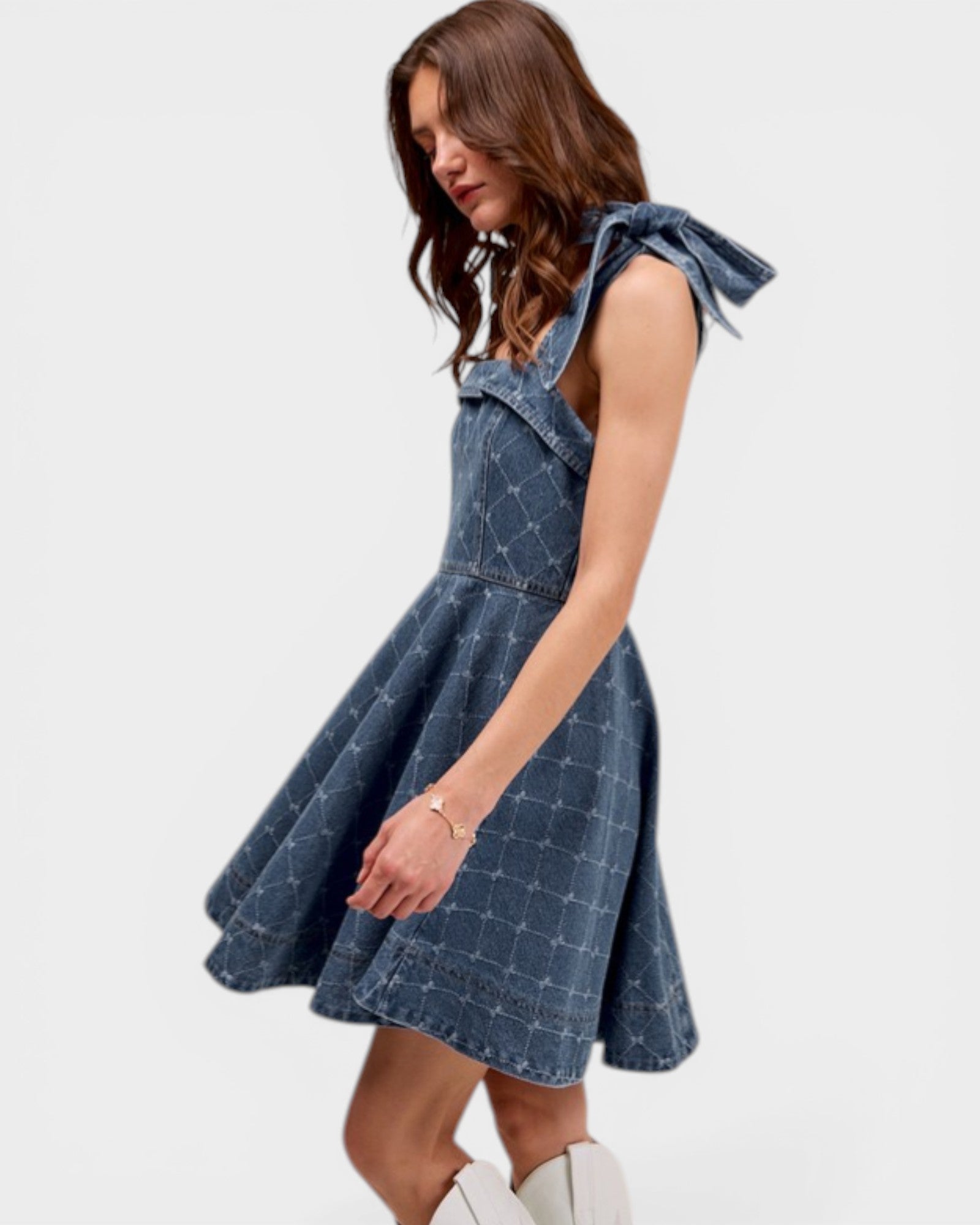 Woman wearing a blue denim dress with bow straps on a white background