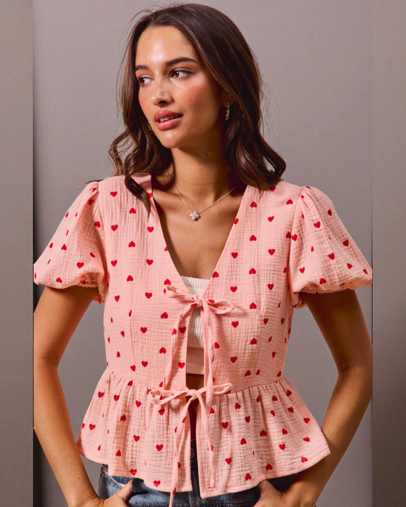 Woman wearing a pink blouse with red heart patterns against a neutral background