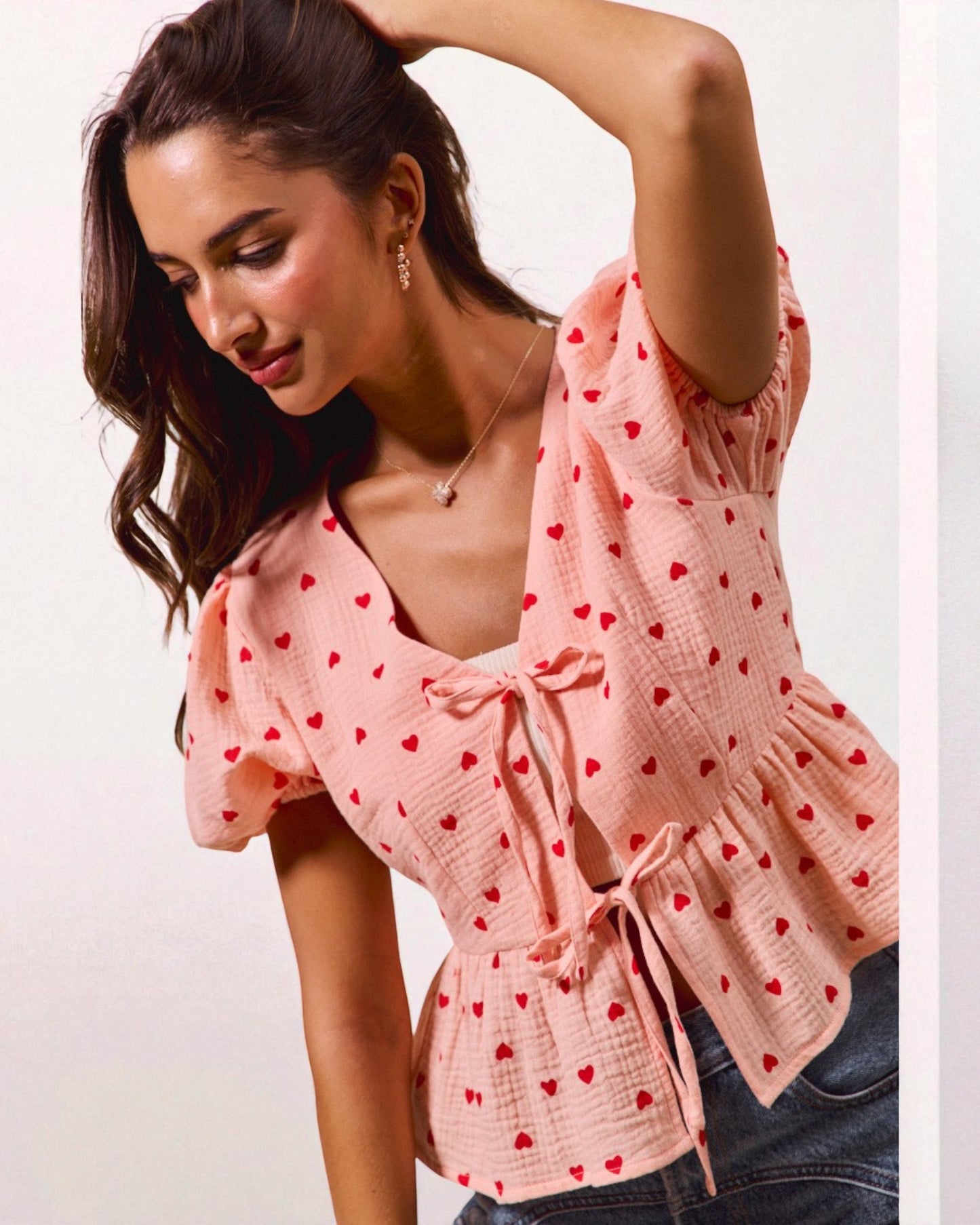 Woman wearing a pink blouse with red heart patterns on a plain background