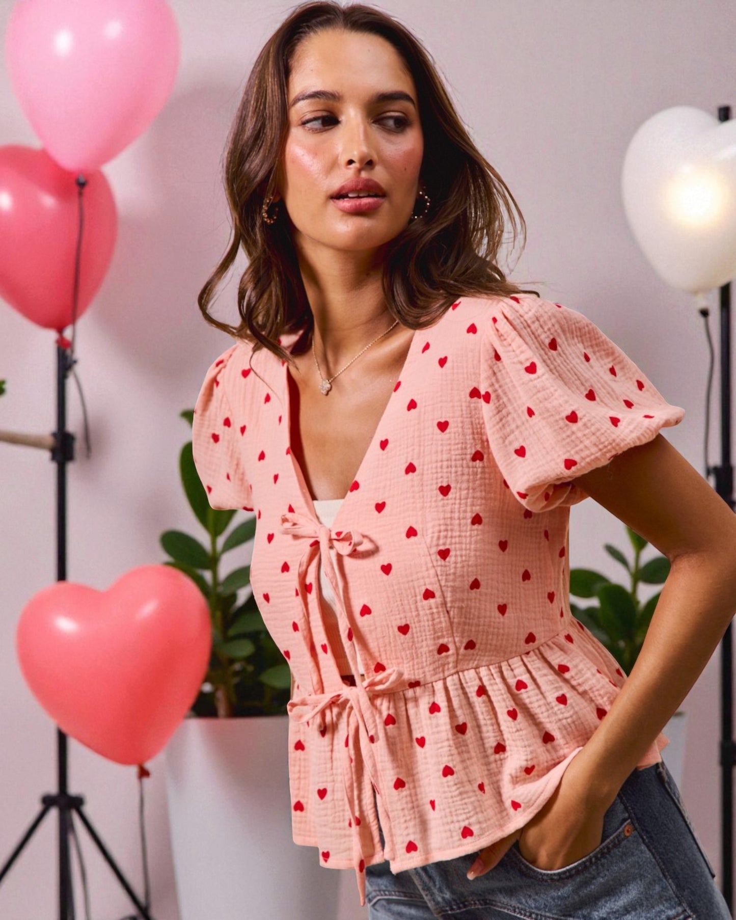 Woman wearing a pink blouse with red heart patterns in a studio setting with balloons.
