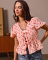 Woman wearing a pink blouse with red heart patterns and blue jeans indoors.