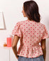 Woman wearing a pink blouse with red heart patterns in a minimal indoor setting.