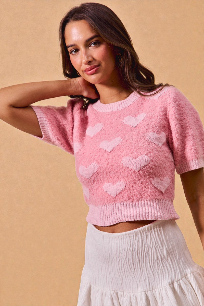 Woman wearing a pink sweater with heart patterns against a beige background