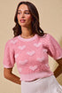 Woman wearing a pink sweater with heart patterns against a beige background
