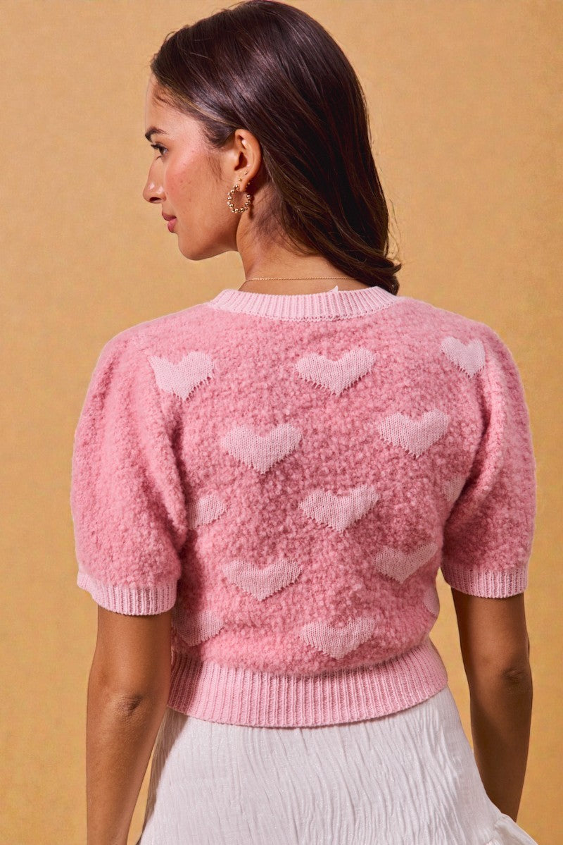 Woman wearing a pink sweater with heart patterns on a beige background