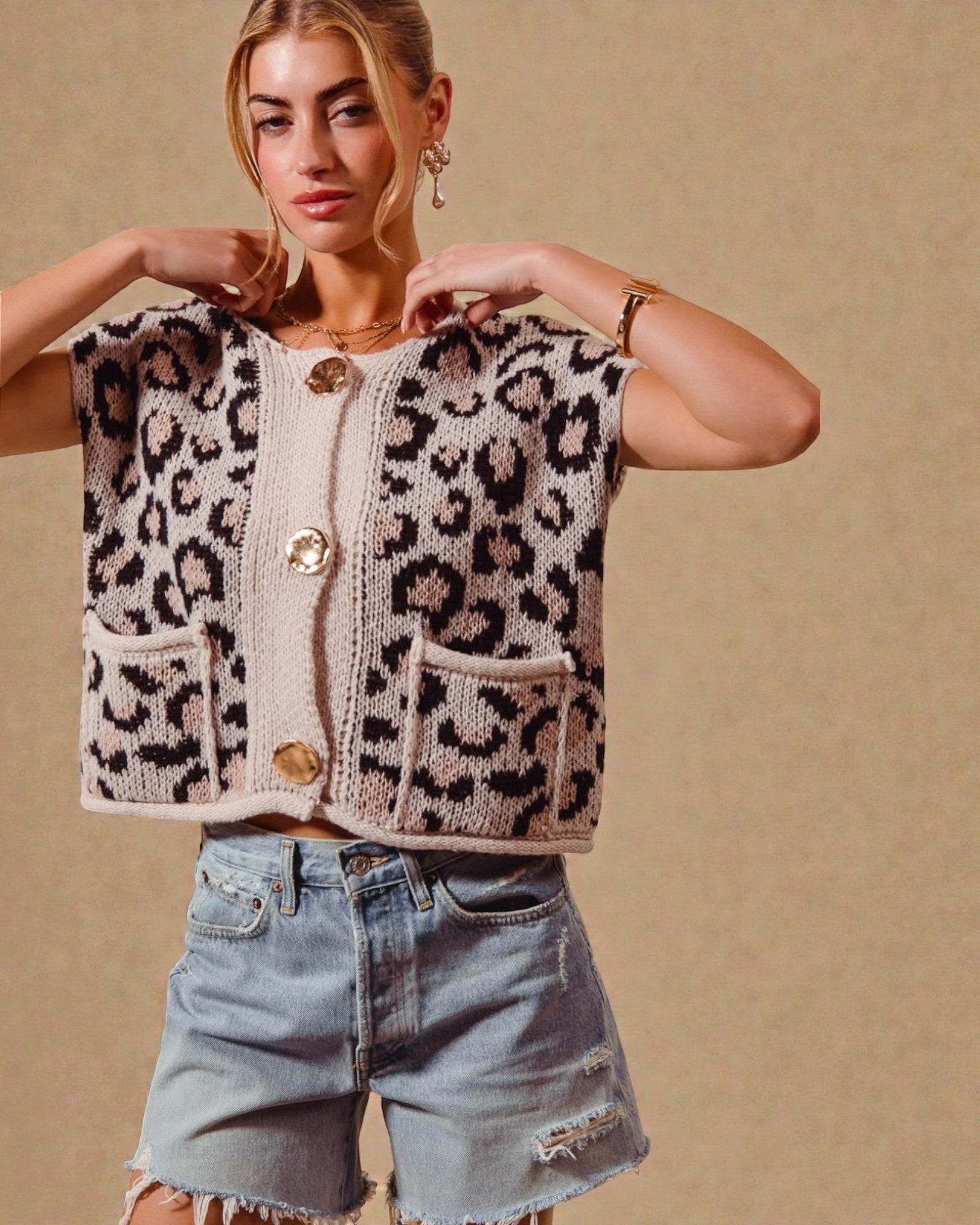 Woman wearing a leopard print vest over a white shirt with denim shorts on a beige background