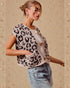 Woman wearing a leopard print vest with gold buttons on a beige background