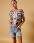 Woman wearing a leopard print cardigan and denim shorts on a beige background