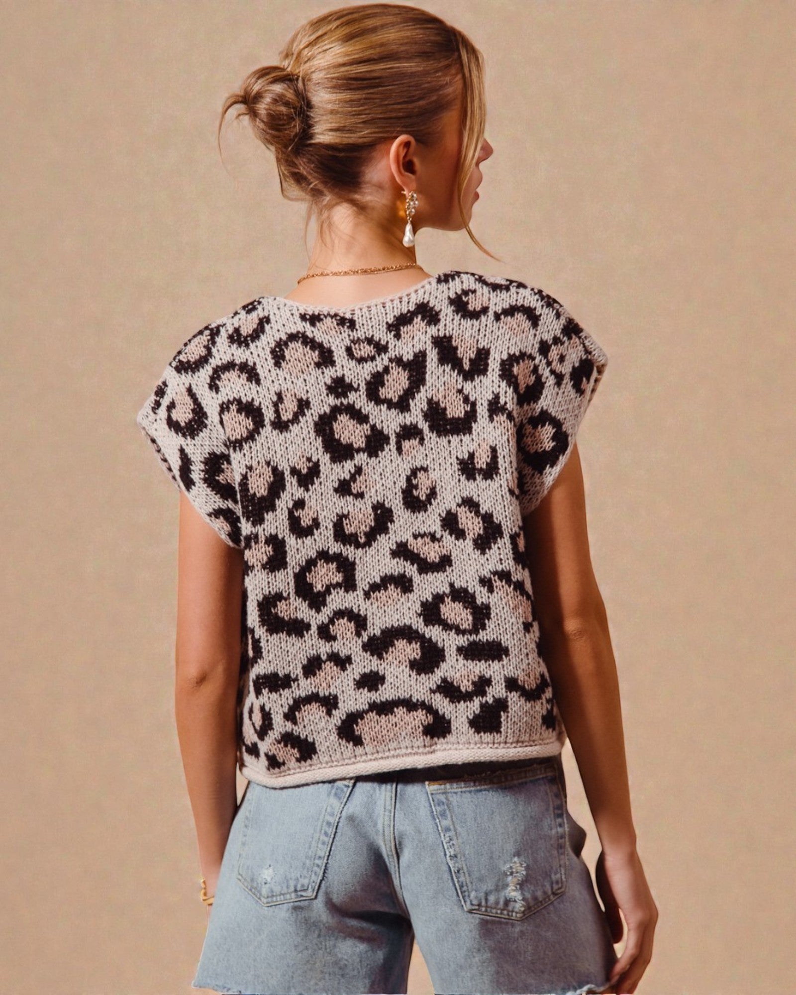 Woman wearing a leopard print top and denim shorts against a beige background
