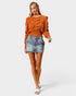 Woman wearing an orange cable knit sweater and denim skirt on a white background