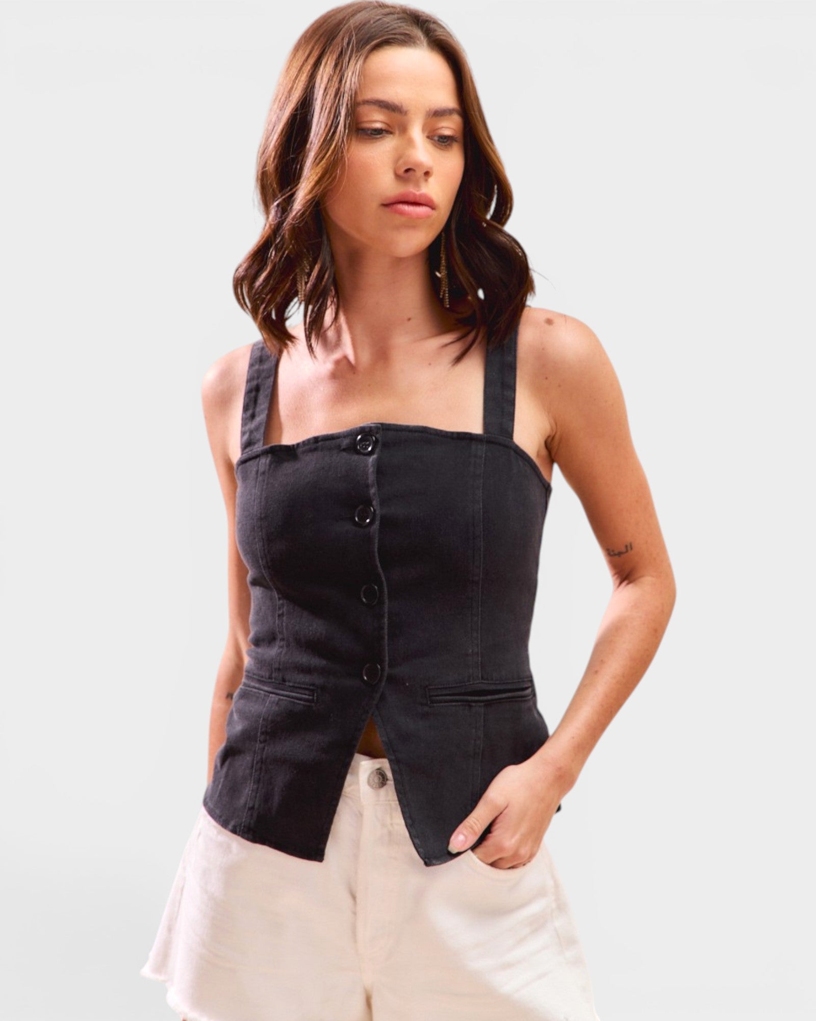 Woman wearing a black sleeveless top with buttons and beige pants on a light gray background