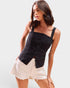 Woman wearing a black sleeveless top with buttons and white shorts on a light background