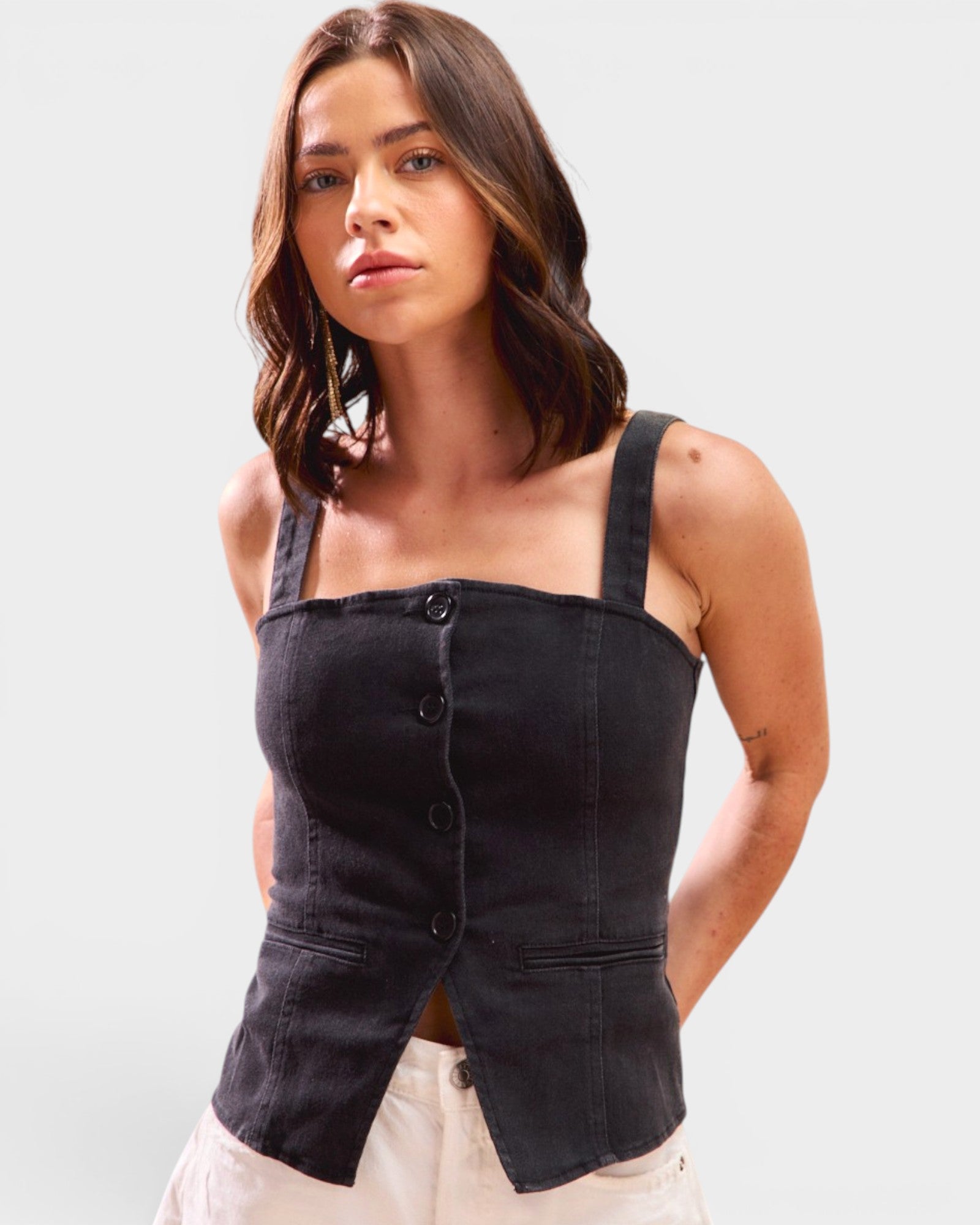 Woman wearing a black sleeveless top with button details on a white background