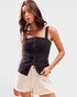 Woman wearing a black sleeveless top and white shorts on a light gray background