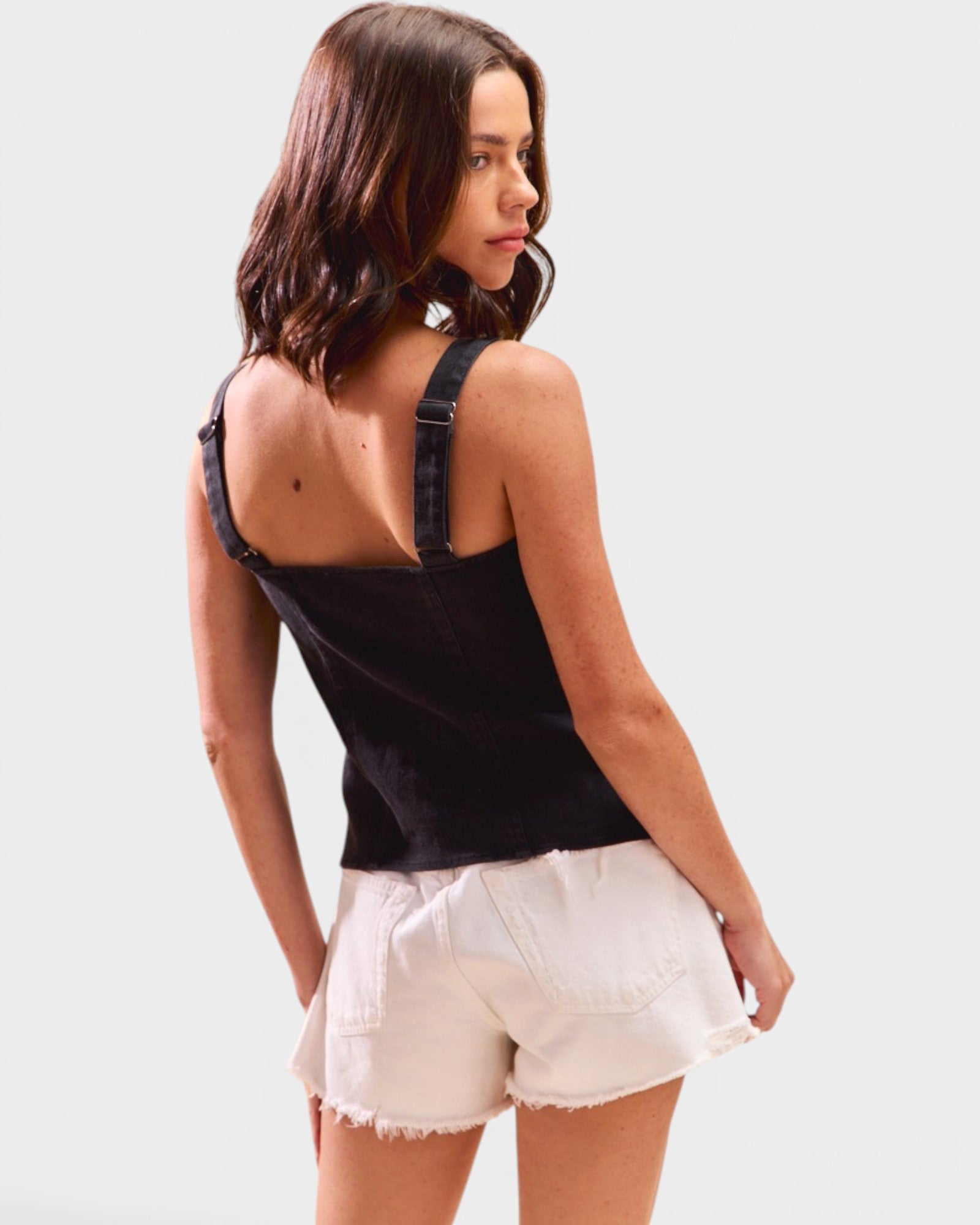 Woman wearing a black tank top with suspenders and white shorts on a light gray background