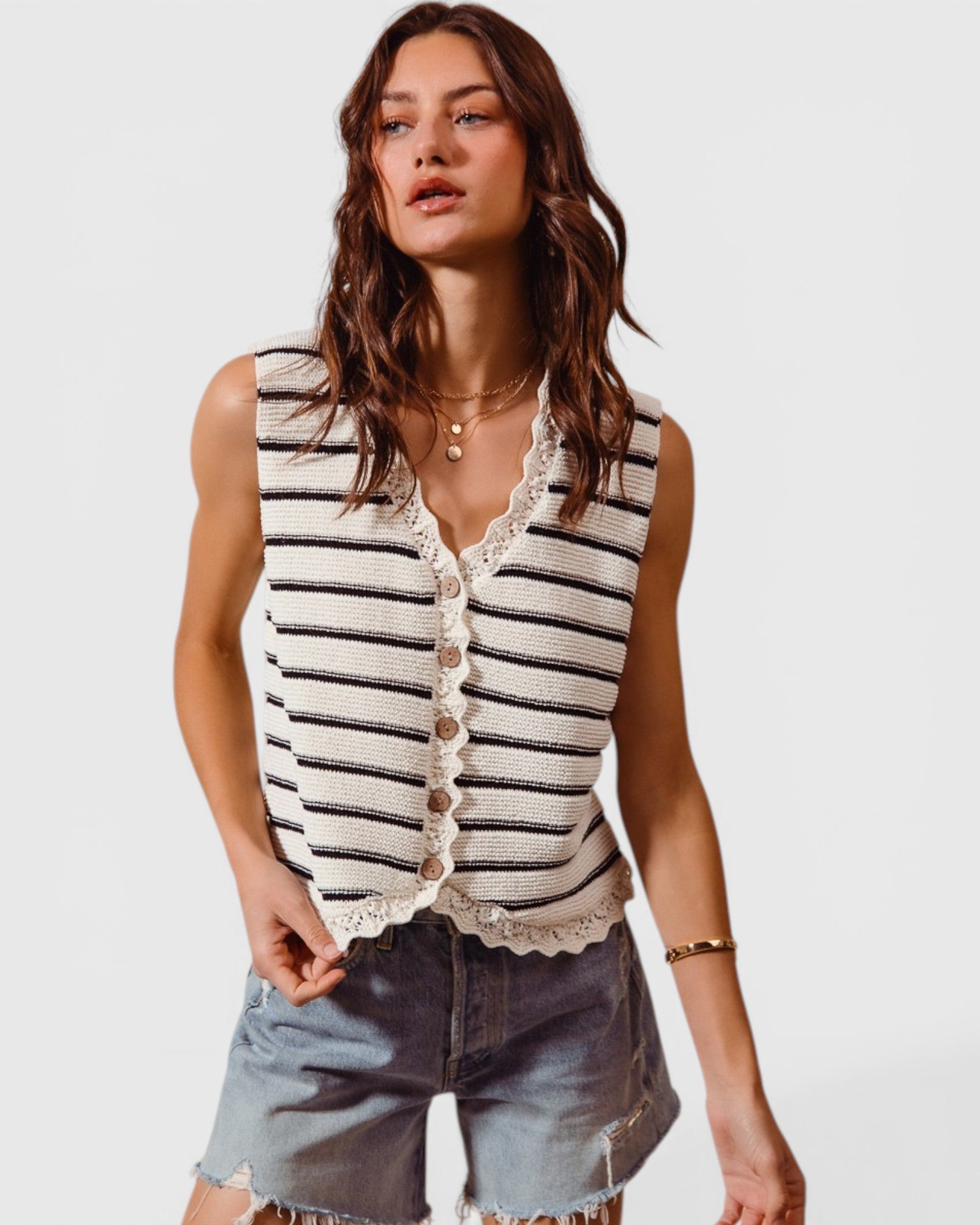 Woman wearing a striped sleeveless top and denim shorts on a plain background