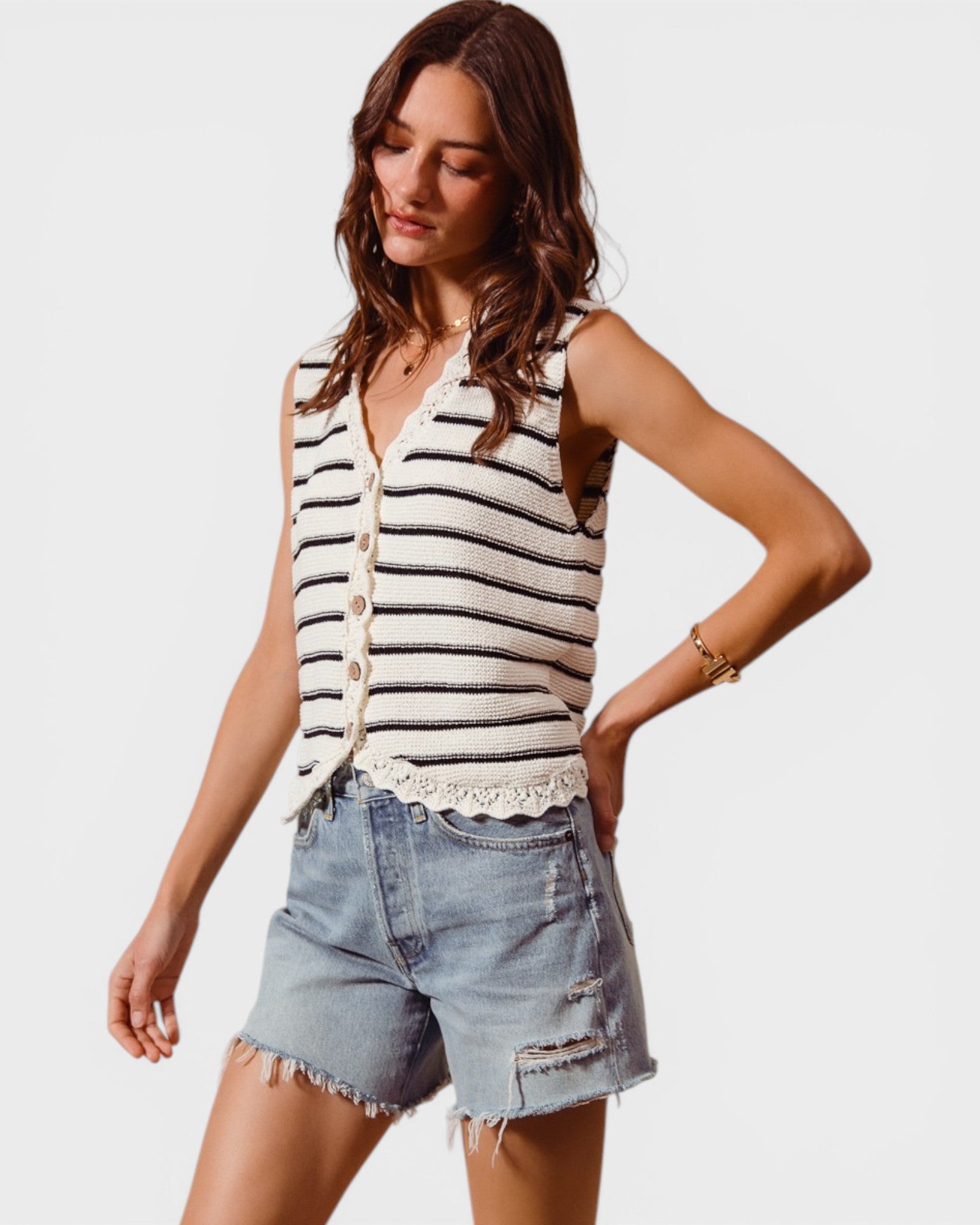 Woman wearing a striped sleeveless top and denim shorts on a plain background