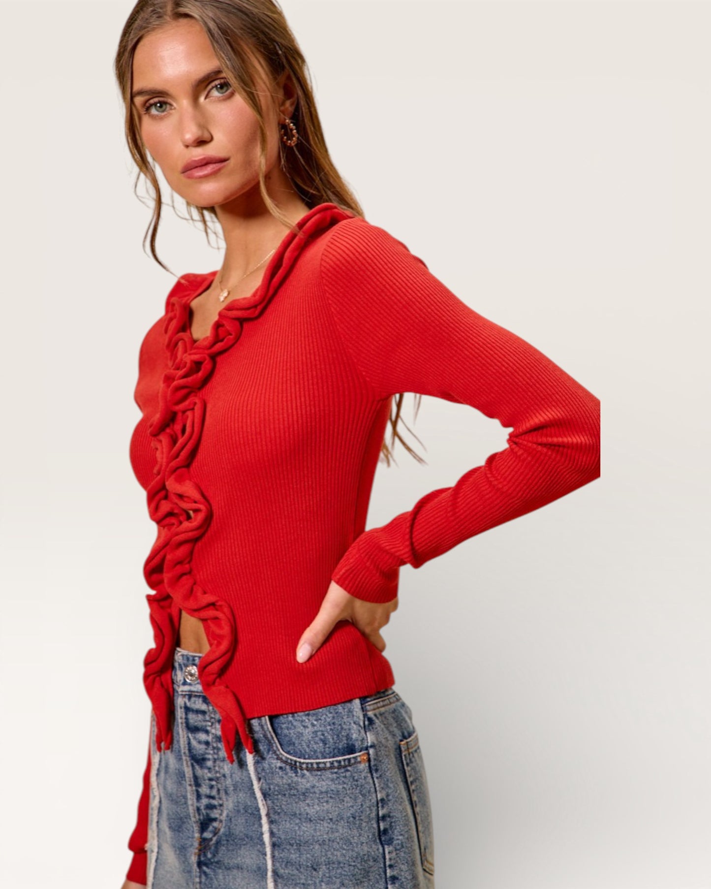 Woman wearing a red ruffled sweater and blue jeans on a white background