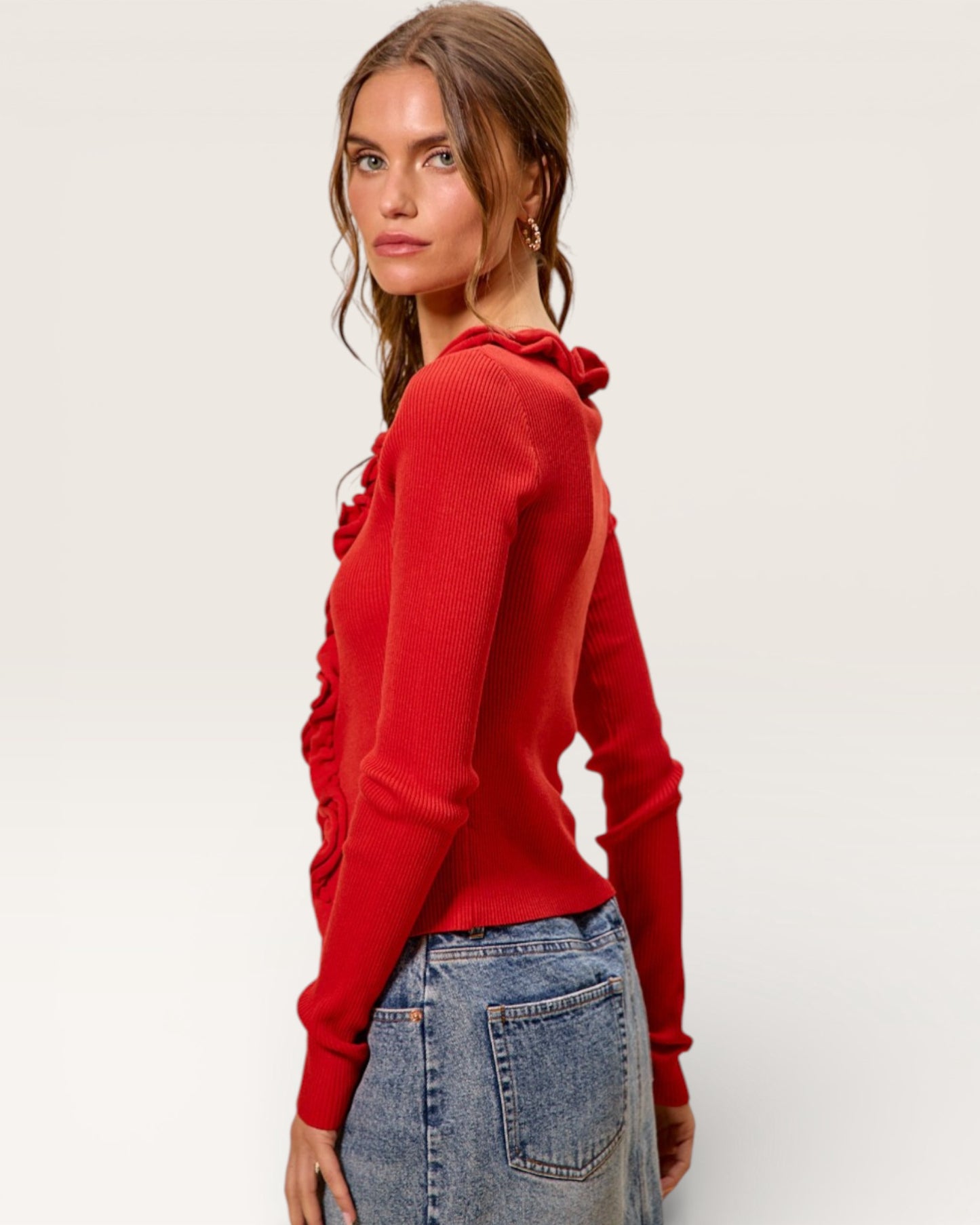 Woman wearing a red sweater with ruffled shoulders against a white background