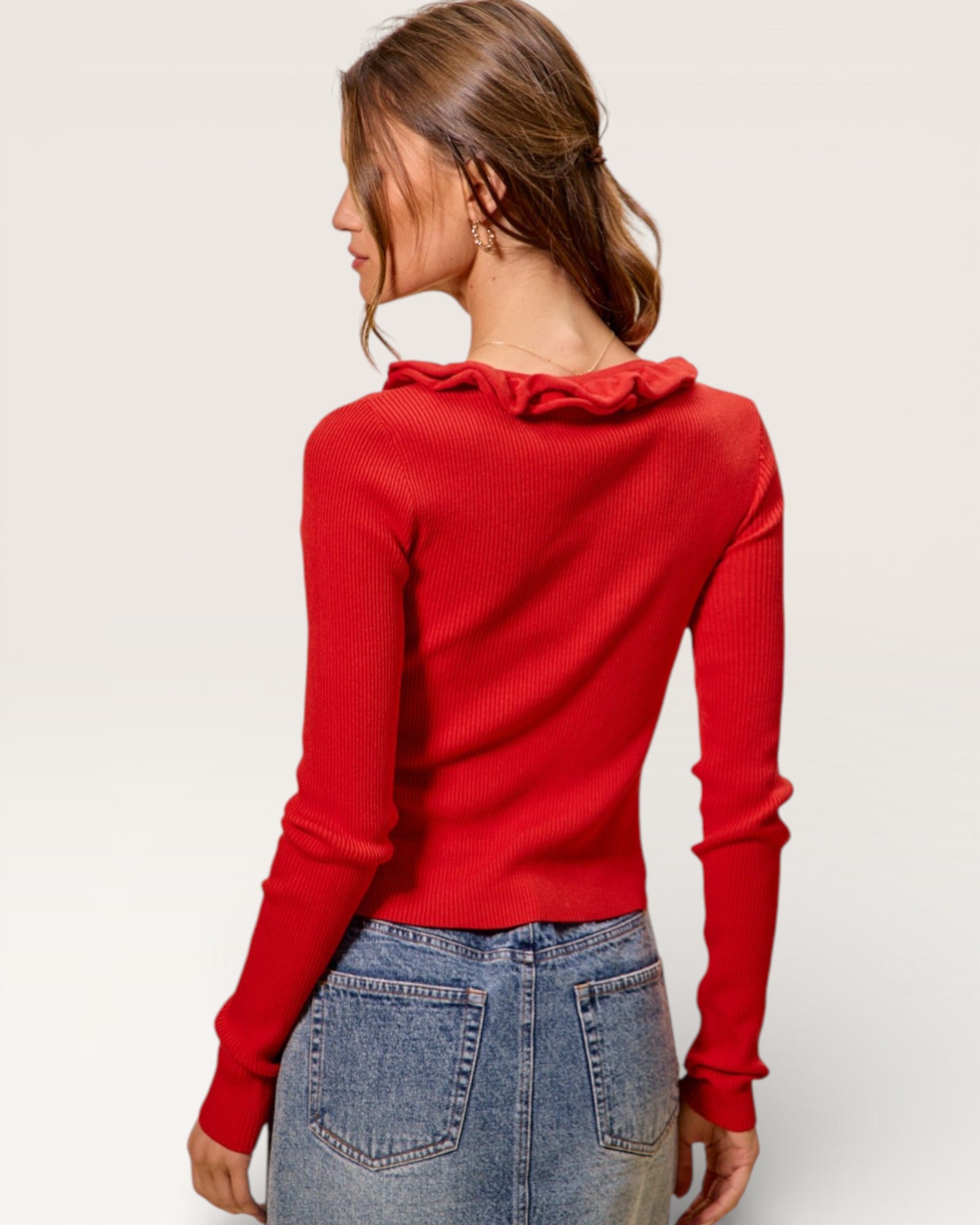 Woman wearing a red sweater with ruffled neckline on a plain background