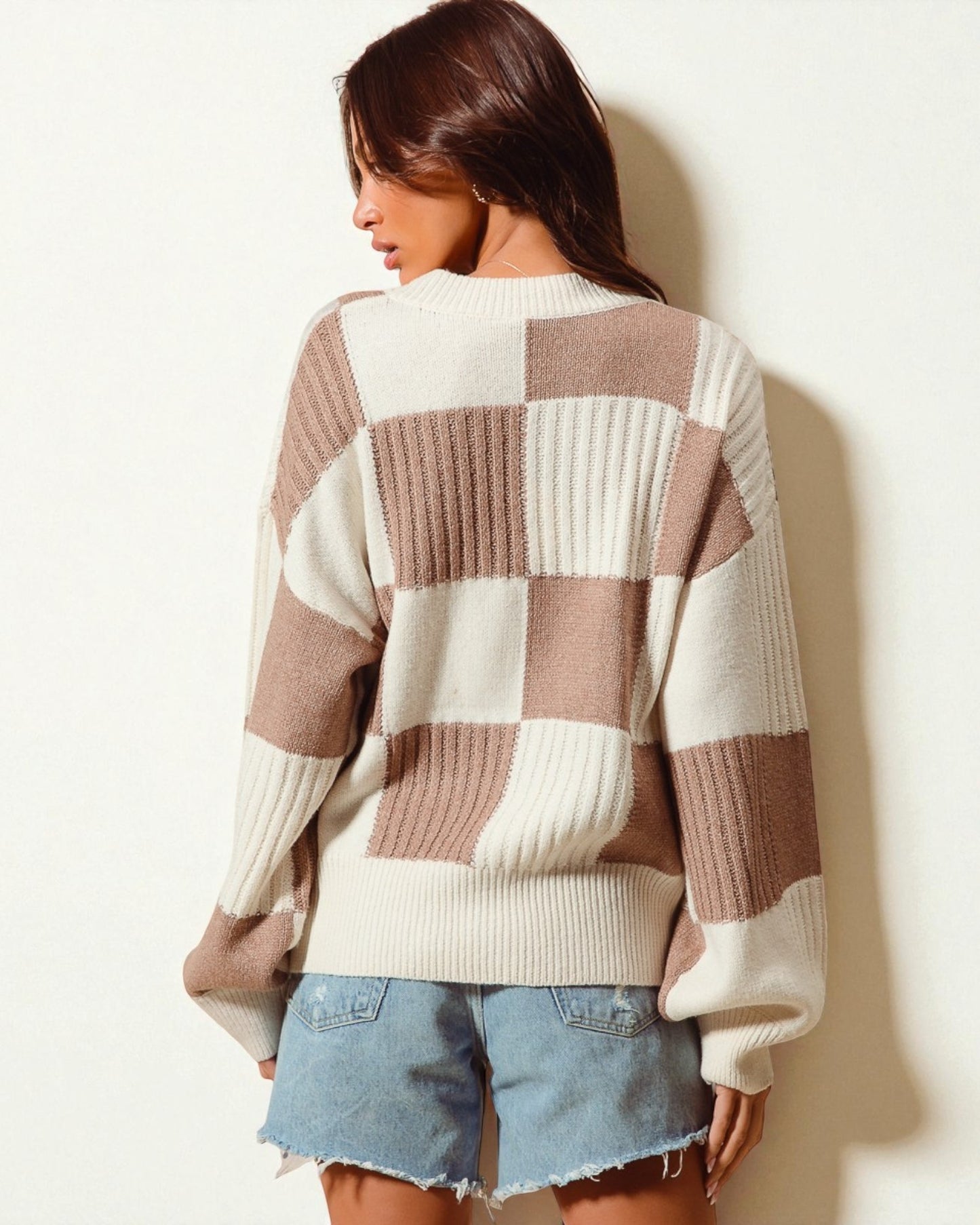 Woman wearing a checkered sweater and denim shorts against a plain background