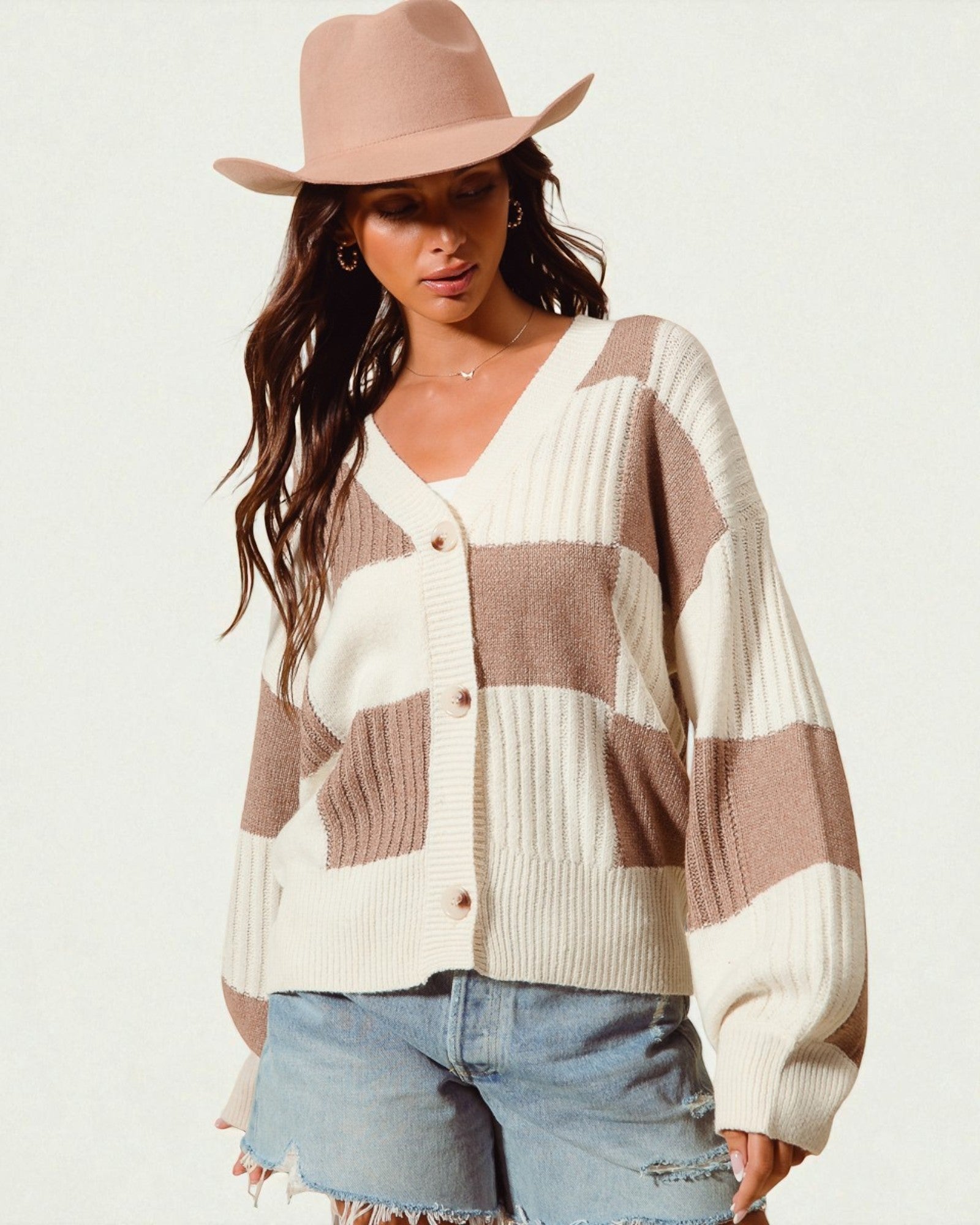 Woman wearing a patterned cardigan and beige hat on a white background